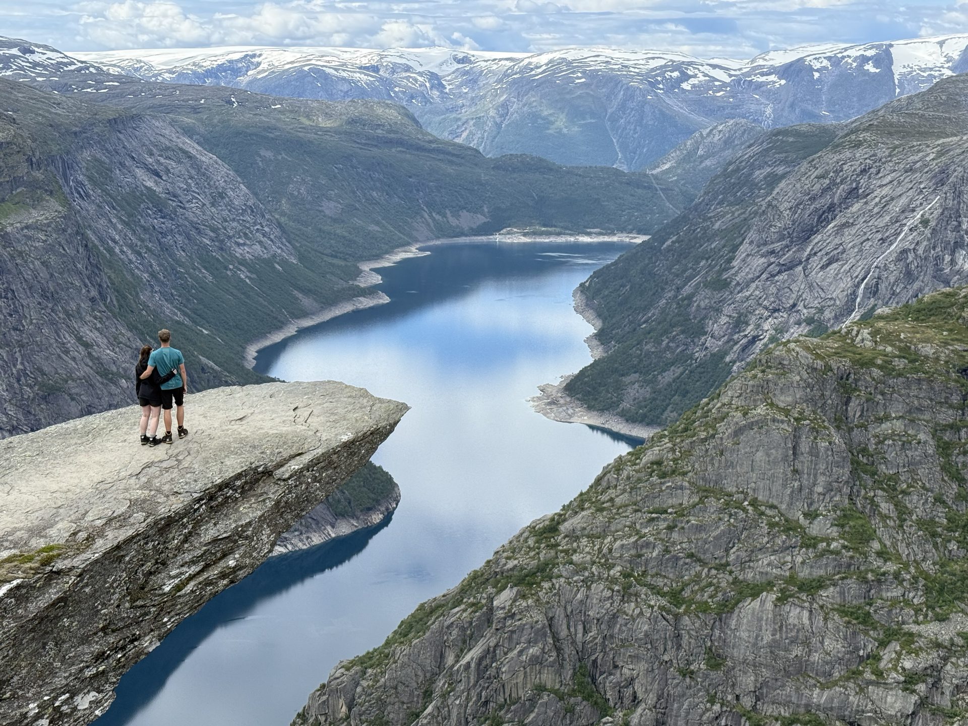Pár cestovatelů sedící na skalním útesu Trolltunga (Trollí jazyk) nad zrcadlovou hladinou fjordu Ringedalsvatnet, ranní mlha — cesta v malé skupině s dovolenanorsko.cz